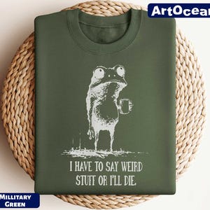 A green t-shirt with a white illustration of a frog holding a mug and the text "I HAVE TO SAY WEIRD STUFF OR ILLDIE" printed on it.