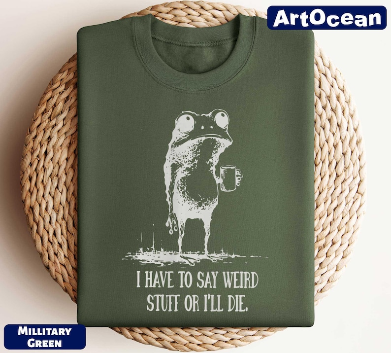 A green t-shirt with a white illustration of a frog holding a mug and the text "I HAVE TO SAY WEIRD STUFF OR ILLDIE" printed on it.