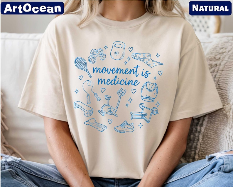 A person wearing a white t-shirt with a graphic design featuring various sports and fitness-related icons, along with the text "movement is medicine".