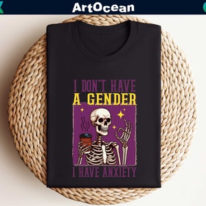 May include: Black t-shirt with a purple graphic of a skeleton holding a coffee cup. The text "I don't have a gender I have anxiety" is printed on the shirt.