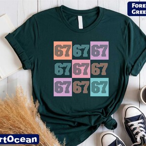 a green t-shirt with a colorful graphic design of numbers on it, along with a pair of sneakers and some other items on a wooden surface.
