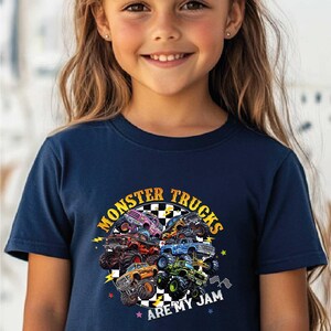 A young girl wearing a navy blue t-shirt with a graphic design of monster trucks and the text "MONSTER TRUCKS ARE MY JAM".