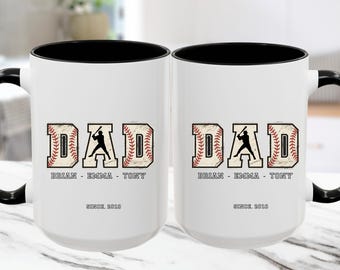 May include: Two white ceramic mugs with black handles and rims. The word "DAD" is printed on each mug in a baseball-themed design, with a baseball and a batter silhouette. The names "BRIAN - EMMA - TONY" and "SINCE 2010" are printed below.