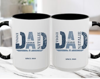 May include: Two white ceramic mugs with black handles and rims. Each mug features the word "DAD" in a distressed blue font, with names and a star below. The text "SINCE. 2019" is printed at the bottom.