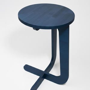 Peut inclure: Une table d'appoint bleu marine avec un plateau rond et un design de pied incurvé unique. La table a une base en forme de croix pour la stabilité. La table est en bois et peinte en bleu marine uni.