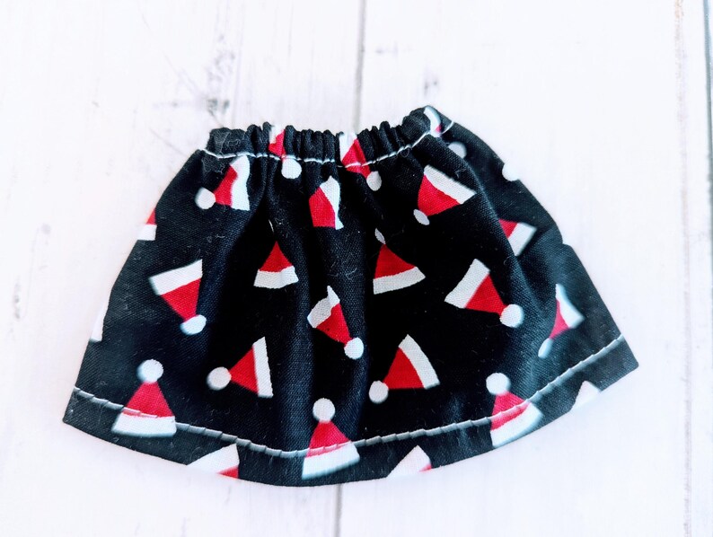 May include: A black skirt with a white and red Santa hat pattern. The skirt has an elastic waistband and is made of a soft, comfortable fabric.