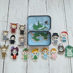 May include: A collection of embroidered character figures from Peter Pan, including Peter Pan, Captain Hook, and Tinkerbell. The figures are arranged around an open, blue tin with a map design inside. The figures are colorful and detailed.