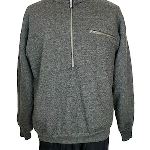 May include: A charcoal gray knit sweater featuring a mock neck collar, a long silver-toned front zipper, and a smaller horizontal zippered pocket on the upper left chest. The garment has long sleeves with ribbed cuffs and a ribbed hem at the waist.