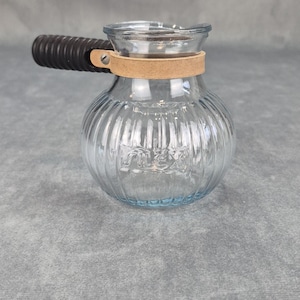 May include: A white ceramic mug with a black handle and the text "But First, Coffee" in a bold, black font. The mug is set against a blurred background, suggesting a cozy setting.