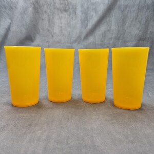 Könnte beinhalten: Ein Set aus vier passenden Trinkgläsern in einer leuchtenden, durchscheinenden gelben Farbe. Jedes Glas hat eine einfache, konisch zulaufende zylindrische Form mit glatter Oberfläche und flachem Boden, aufgereiht vor einem neutralen grauen Hintergrund.
