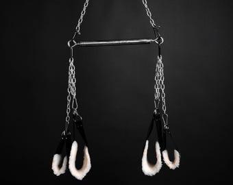 以下が含まれることがあります： 黒い金属製のブランコセットで、白いファーの袖口がチェーンからぶら下がっています。ブランコセットは天井から吊り下げられています。