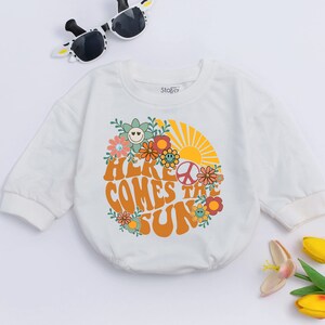 May include: White long-sleeved baby onesie with a graphic print of a sun with flowers and the text "Here Comes the Sun".