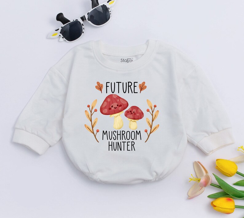 Puede incluir: Mono blanco de manga larga para beb&eacute; con un gr&aacute;fico de dos setas de dibujos animados y el texto "FUTURE MUSHROOM HUNTER".