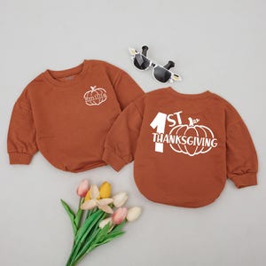 May include: Two brown long-sleeved shirts with a pumpkin design. One shirt says "1st Thanksgiving" and the other says "Emilie".