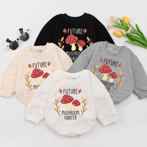 Puede incluir: Cuatro bodies de beb&eacute; en diferentes colores con un gr&aacute;fico de hongo y el texto "Future Mushroom Hunter". Los bodies son de color crema, blanco, negro y gris.
