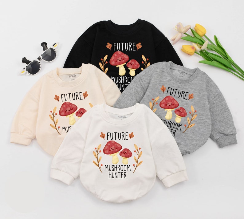 Puede incluir: Cuatro bodies de beb&eacute; en diferentes colores con un gr&aacute;fico de hongo y el texto "Future Mushroom Hunter". Los bodies son de color crema, blanco, negro y gris.