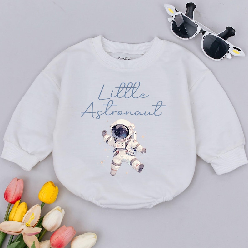 May include: White long-sleeve onesie with a blue astronaut graphic and the text "Little Astronaut".