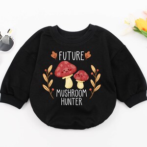 Puede incluir: Sudadera negra de manga larga con un gr&aacute;fico blanco de dos setas y el texto "FUTURE MUSHROOM HUNTER".