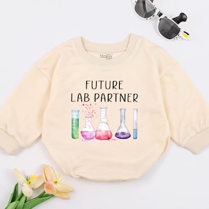 May include: A cream colored long-sleeved onesie with the text "FUTURE LAB PARTNER" and a watercolor illustration of beakers and test tubes.