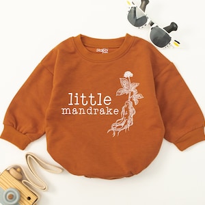May include: A brown long-sleeve onesie with a white graphic of a mandrake plant and the text "little mandrake".