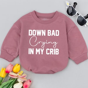 May include: A pink long-sleeved sweatshirt with the text "Down Bad Crying In My Crib" in white.