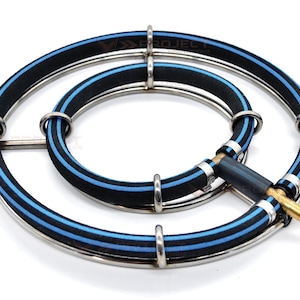 May include: A circular gas burner assembly featuring two concentric rings made of black rubber tubing with a central blue stripe. The rings are held in place by silver metal clips and connected to a brass-colored nozzle fitting at the side.