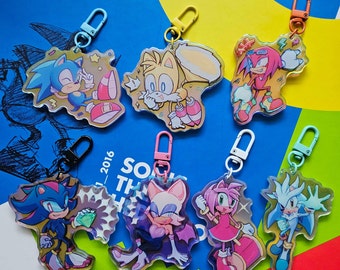 Könnte beinhalten: Sieben bunte Schlüsselanhänger mit Charakteren aus der Videospiel-Reihe Sonic the Hedgehog. Die Schlüsselanhänger sind aus klarem Acryl und zeigen die Charaktere Sonic, Tails, Knuckles, Shadow, Rouge, Amy und Silver.