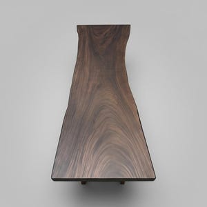 Puede incluir: Mesa de madera marr&oacute;n oscuro con borde natural. La mesa tiene un borde natural y org&aacute;nico en un lado y un borde liso y recto en el otro. La veta de la madera es visible. La mesa est&aacute; soportada por patas peque&ntilde;as y oscuras. Mide unos 180 cm de largo.