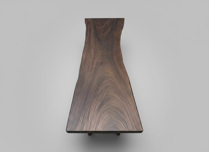 Puede incluir: Mesa de madera marr&oacute;n oscuro con borde natural. La mesa tiene un borde natural y org&aacute;nico en un lado y un borde liso y recto en el otro. La veta de la madera es visible. La mesa est&aacute; soportada por patas peque&ntilde;as y oscuras. Mide unos 180 cm de largo.