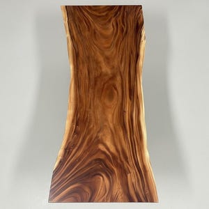 Puede incluir: Una losa de madera rectangular con borde vivo y forma natural y org&aacute;nica. La veta de la madera presenta un color marr&oacute;n c&aacute;lido y rico con patrones arremolinados m&aacute;s oscuros. Ideal para una mesa o encimera.