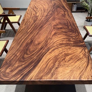 Puede incluir: Una gran tapa de mesa rectangular de madera de color marrón oscuro con intrincados patrones de veta. La madera tiene un acabado natural y pulido.