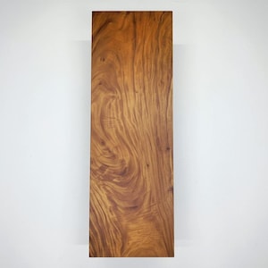 Puede incluir: Una tabla de madera rectangular con un color marr&oacute;n c&aacute;lido y rico y un patr&oacute;n de vetas de madera prominente. La veta de la madera presenta patrones arremolinados y variaciones de tono, creando una apariencia natural y texturizada. Sobre fondo blanco.
