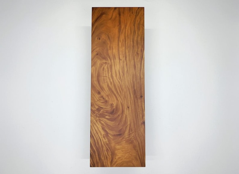 Puede incluir: Una tabla de madera rectangular con un color marr&oacute;n c&aacute;lido y rico y un patr&oacute;n de vetas de madera prominente. La veta de la madera presenta patrones arremolinados y variaciones de tono, creando una apariencia natural y texturizada. Sobre fondo blanco.