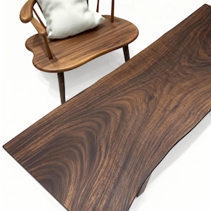 Puede incluir: Una silla de madera con un coj&iacute;n blanco y una mesa larga de madera oscura. La silla tiene respaldo y reposabrazos curvos. La mesa tiene un borde natural y una veta de madera rica y oscura. Los muebles est&aacute;n sobre un fondo blanco.