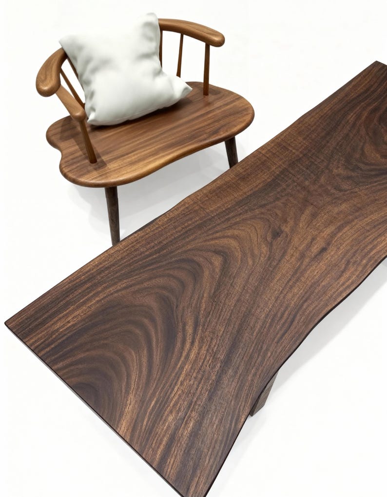 Puede incluir: Una silla de madera con un coj&iacute;n blanco y una mesa larga de madera oscura. La silla tiene respaldo y reposabrazos curvos. La mesa tiene un borde natural y una veta de madera rica y oscura. Los muebles est&aacute;n sobre un fondo blanco.