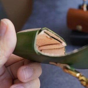 以下が含まれることがあります： 緑色の革製のケースで、フラップを開けると、層状の内部が見える。ケースは高品質の革で作られており、頑丈な構造をしている。