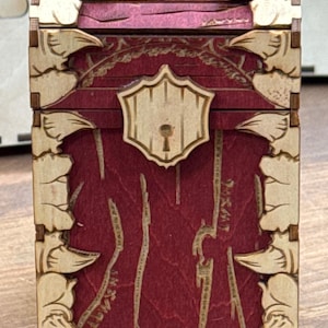 K&ouml;nnte beinhalten: Eine Holzkiste mit einer roten gebeizten Oberfl&auml;che und einem dekorativen Schloss. Die Kiste hat ein geschnitztes Design auf der Vorder- und den Seitenfl&auml;chen.