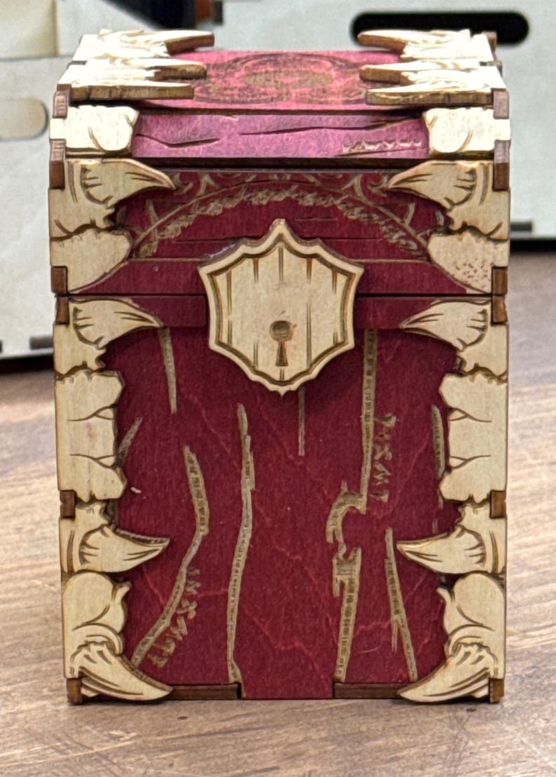K&ouml;nnte beinhalten: Eine Holzkiste mit einer roten gebeizten Oberfl&auml;che und einem dekorativen Schloss. Die Kiste hat ein geschnitztes Design auf der Vorder- und den Seitenfl&auml;chen.