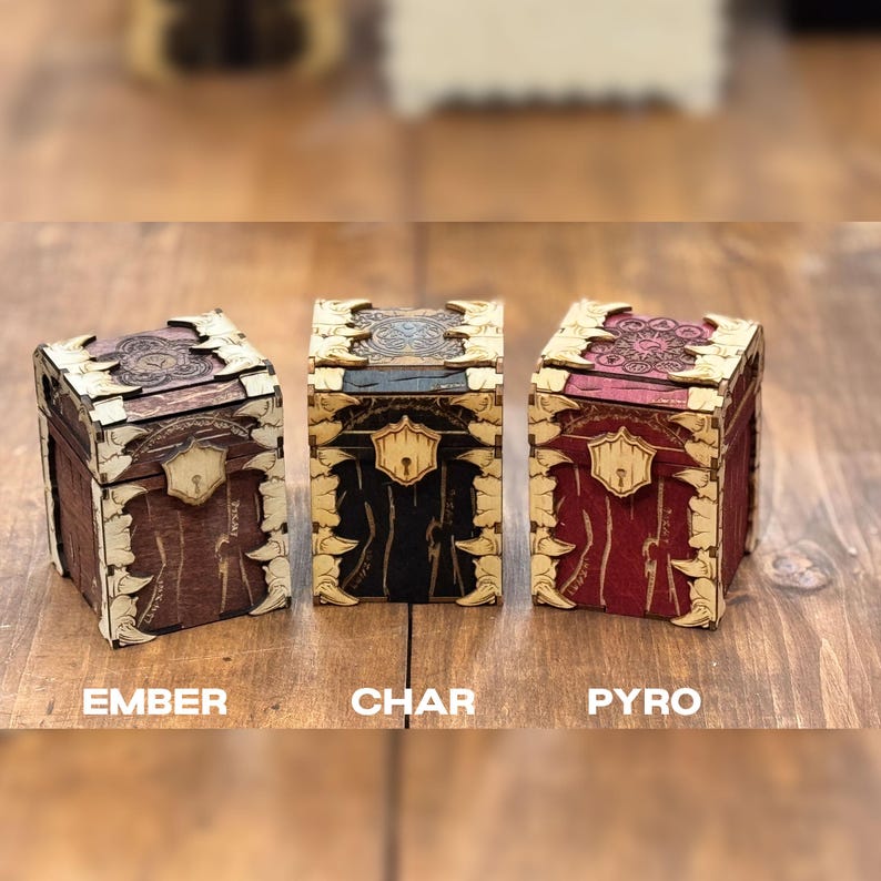 K&ouml;nnte beinhalten: Drei Holzkisten mit aufwendigen Designs und einem Verschluss. Die Kisten sind mit "Ember", "Char" und "Pyro" beschriftet.