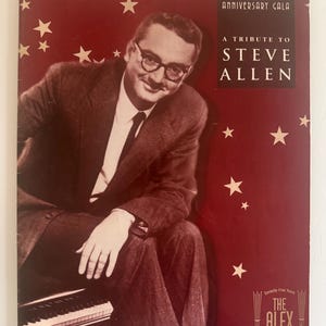 Peut inclure: Un programme rectangulaire pour le 75e anniversaire du Alex Theatre, avec un portrait de Steve Allen en costume et lunettes. La couverture rouge foncé est décorée d'étoiles blanches et porte le texte : A Tribute to Steve Allen, Sunday, May 20, 2001.