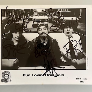 May include: Black and white photograph of the band Fun Lovin' Criminals in a car, with signatures across the image. The band members are in the front seat, with a city street in the background. The band's logo and the words "Fun Lovin' Criminals" are printed at the bottom.