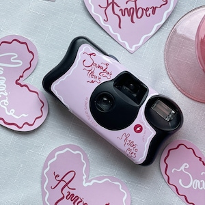 May include: A black disposable camera with a pink and white heart-shaped sticker that says "Savana's Hen's" and "47 Days Until I Do!"  The camera also has a sticker that says "Miss to Mrs".