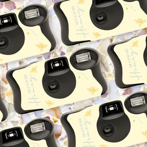 May include: A collection of black disposable cameras with a light yellow face. The cameras have the text "SHE FOUND HER Honey" and bee graphics. The background is a speckled, multi-colored surface.