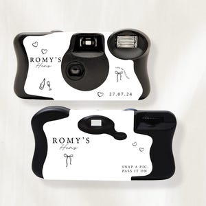 May include: Two black and white disposable cameras. The cameras have the text "ROMY'S Hens" and the date "27.07.24" printed on them. One camera has the text "SNAP A PIC. PASS IT ON". The cameras feature heart and bow graphics.