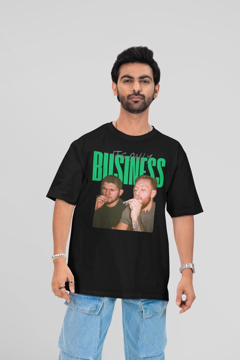 May include: Black t-shirt featuring a graphic of two men with cigarettes, with the text "IT'S ONLY BUSINESS" in green. The shirt is worn by a person with a beard, bracelets, and a watch.
