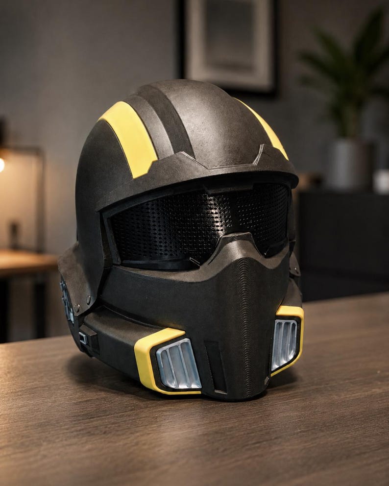 May include: A matte black full-face helmet featuring two prominent yellow stripes running over the top, a dark mesh visor, and a lower face guard with silver-coloured vents framed by yellow accents on both the left and right sides of the chin.