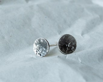 May include: A pair of silver earrings with a hammered, textured finish. The earrings are round and have a slightly irregular shape.