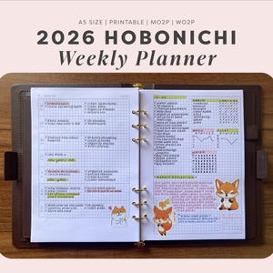 May include: A 2026 Hobonichi weekly planner in an A5 size, featuring a grid layout with handwritten to-do lists, habit trackers, and fox stickers. The open planner is held in a dark brown leather cover with gold-toned metal ring binding.