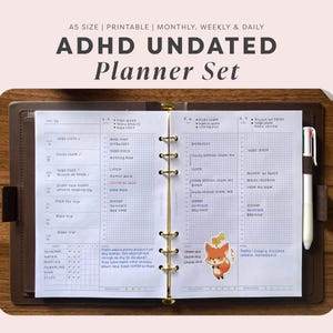 Puede incluir: Una agenda sin fecha tamaño A5 abierta en una carpeta marrón con anillas doradas. Las páginas blancas presentan un diseño de cuadrícula para la planificación diaria, semanal y mensual con tareas escritas a mano y una pegatina de un zorro.