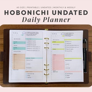 Op de afbeelding: Een ongedateerde dagplanner van A5-formaat in een bruine lederen map met gouden ringen. De open pagina's hebben een rasterindeling met secties voor takenlijsten, maaltijdplannen en dagelijkse routines, gemarkeerd met pastelkleurige stiften.